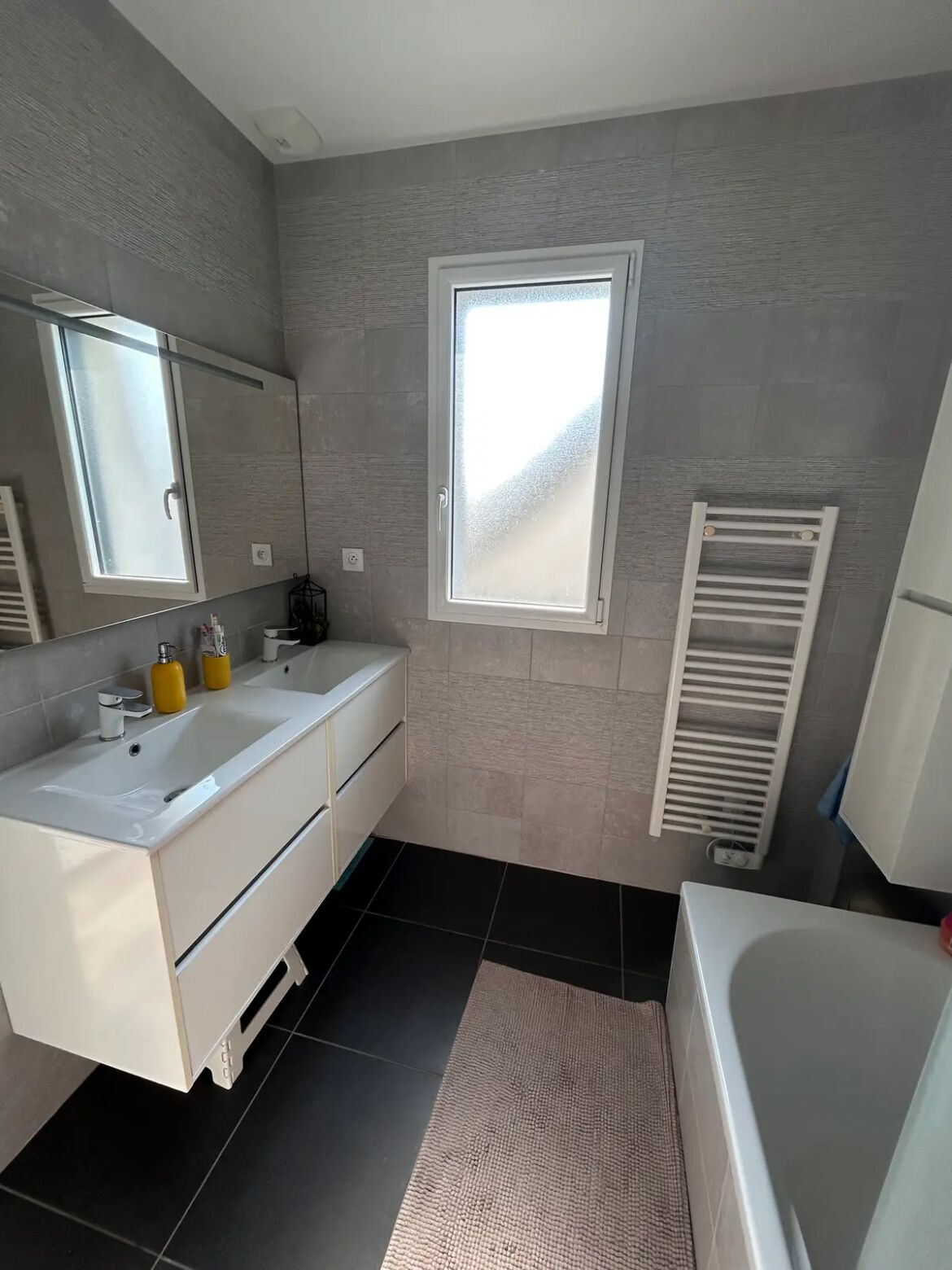 A modern bathroom with a large mirror, a bathtub, a sink with toiletries, and a window.