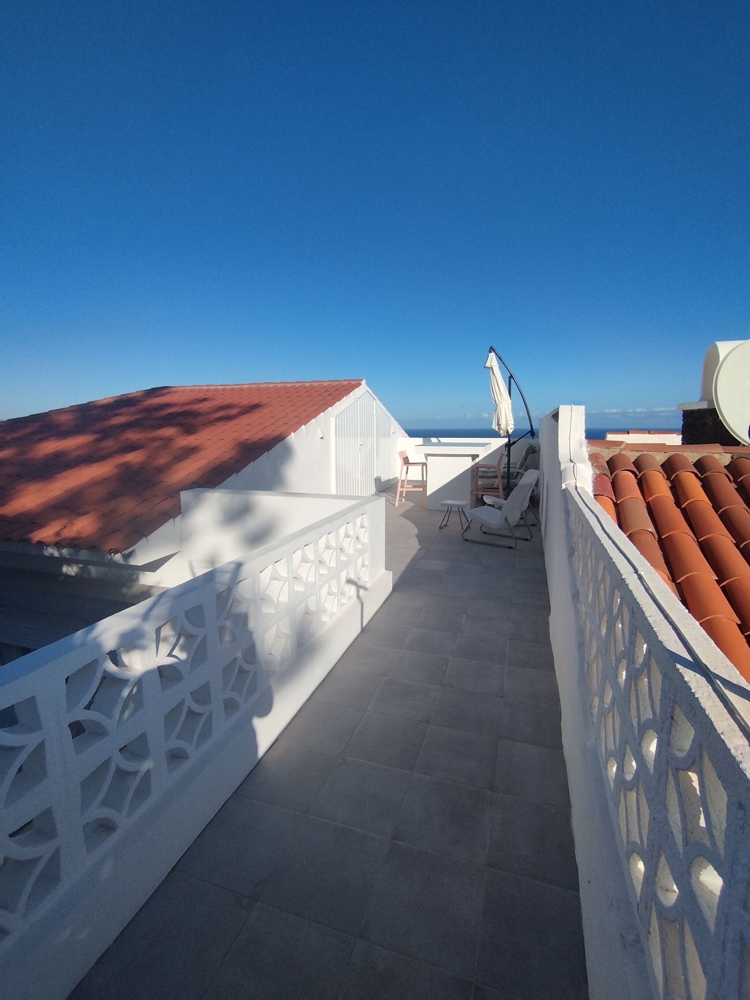 Une terrasse sur le toit offrant une vue dégagée sur la mer, avec une balustrade blanche et un toit recouvert de tuiles rouges.