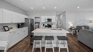 A modern kitchen with white cabinets, a central island with bar stools, a built-in oven, and a microwave. - Newly built Chalet on State Park Golf Course 5 min from Pickwick Lake! (Counce)