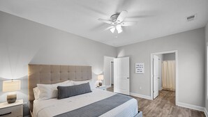 A bedroom with a large bed, a ceiling fan, and a door leading to a bathroom. - Newly built Chalet on State Park Golf Course 5 min from Pickwick Lake! (Counce)