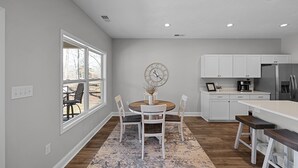 A modern kitchen with white cabinetry, a round dining table, and a large window. - Newly built Chalet on State Park Golf Course 5 min from Pickwick Lake! (Counce)