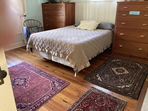 A bedroom with a bed, two wooden dressers, and two rugs on the floor.