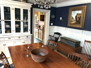 Comedor con mesa de madera, sillas, un tazón grande y una alacena con puertas de vidrio.