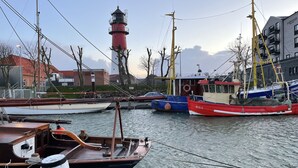 A harbor with boats docked, a lighthouse, and buildings in the background. - Gemütliche Ferienwohnung Mitten im Zentrum von Büsum (Büsum)