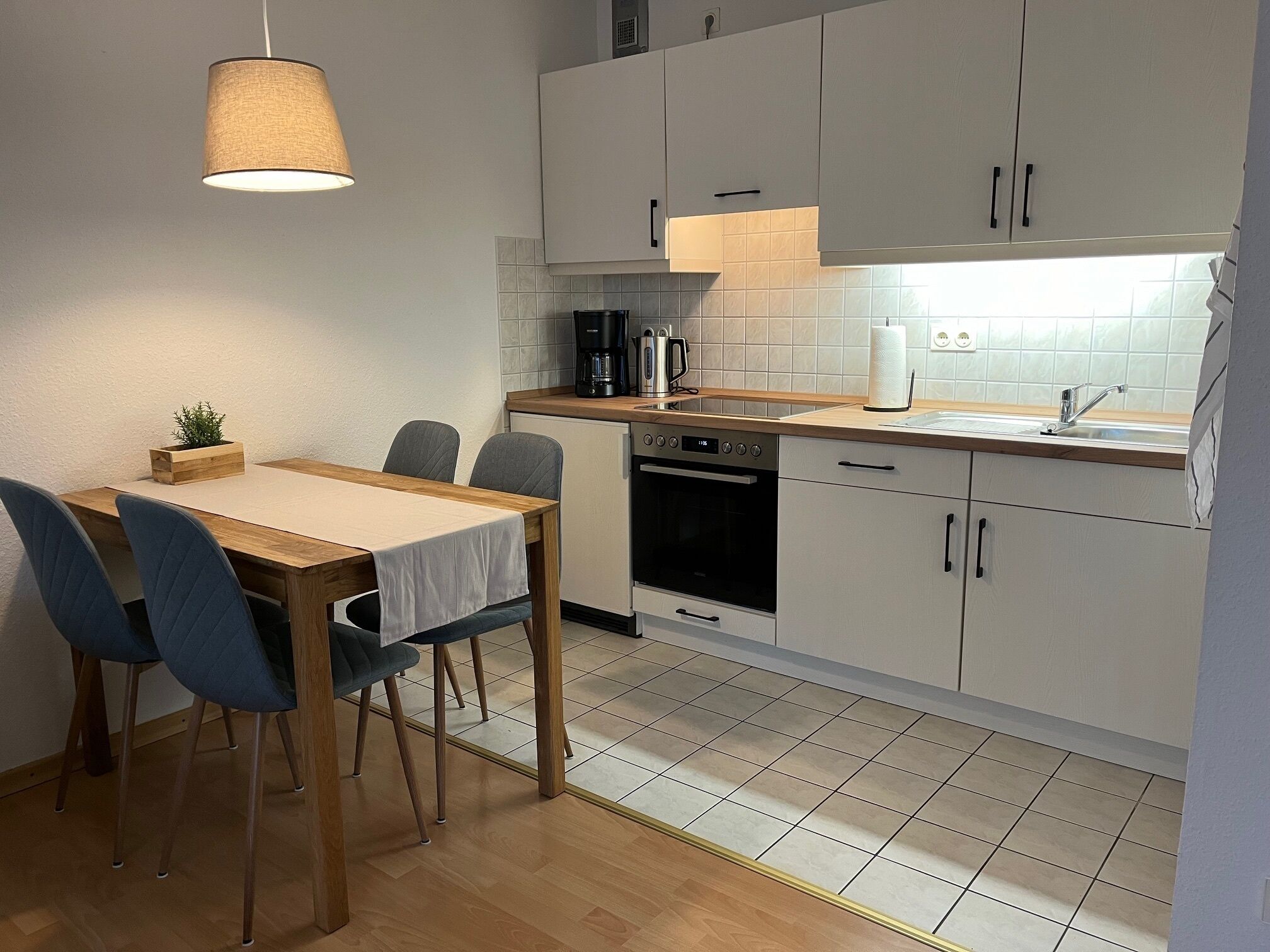Une cuisine compacte avec un coin repas, comprenant une table en bois, des chaises, une machine à café et un évier.