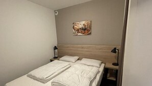 A hotel room with a bed, two bedside tables, a wall-mounted lamp, and a painting.