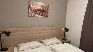 Una cama bien hecha con ropa blanca, dos mesitas de noche con lámparas y un cuadro enmarcado en la pared.