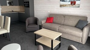 Una sala moderna con sofá, sillones, una mesita de centro y una cocina al fondo.