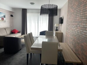 A modern hotel room with a dining area, a sofa, a TV, and a brick accent wall.