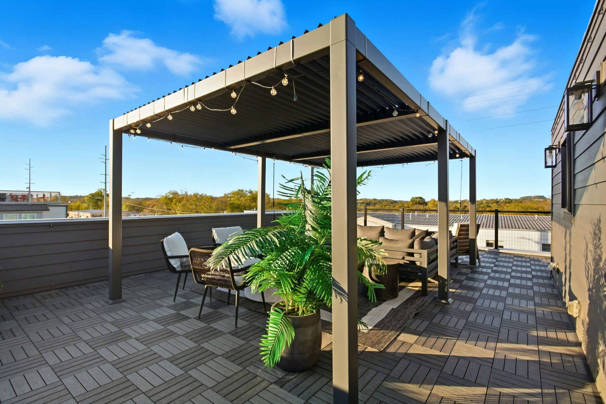 An outdoor patio with a pergola, seating, and a potted plant.