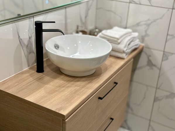 A bathroom with a white marble sink, black faucet, and wooden cabinetry.