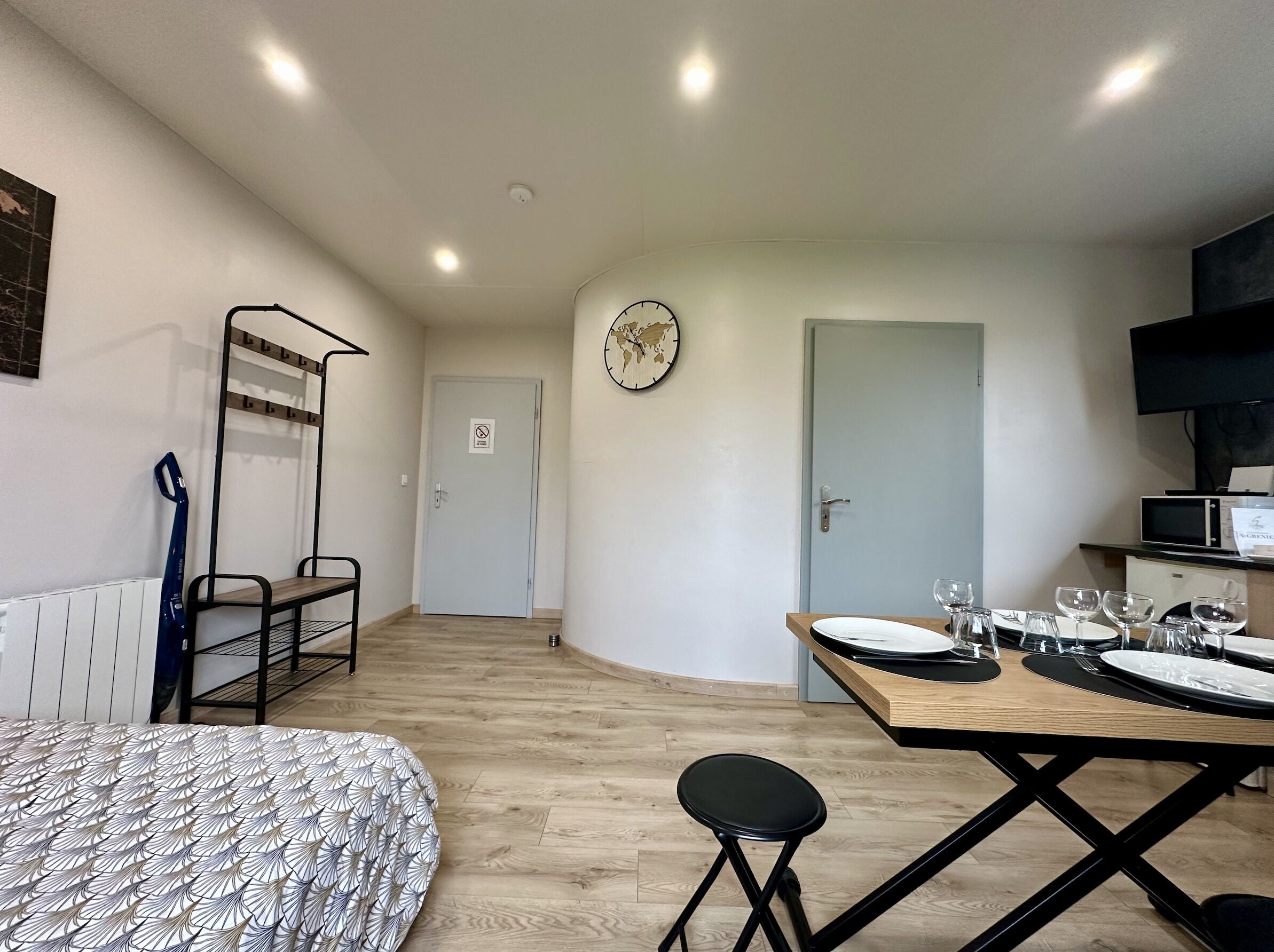 Ein kleines Hotelzimmer mit Bett, Schreibtisch mit Stuhl, Mikrowelle und Fernseher.