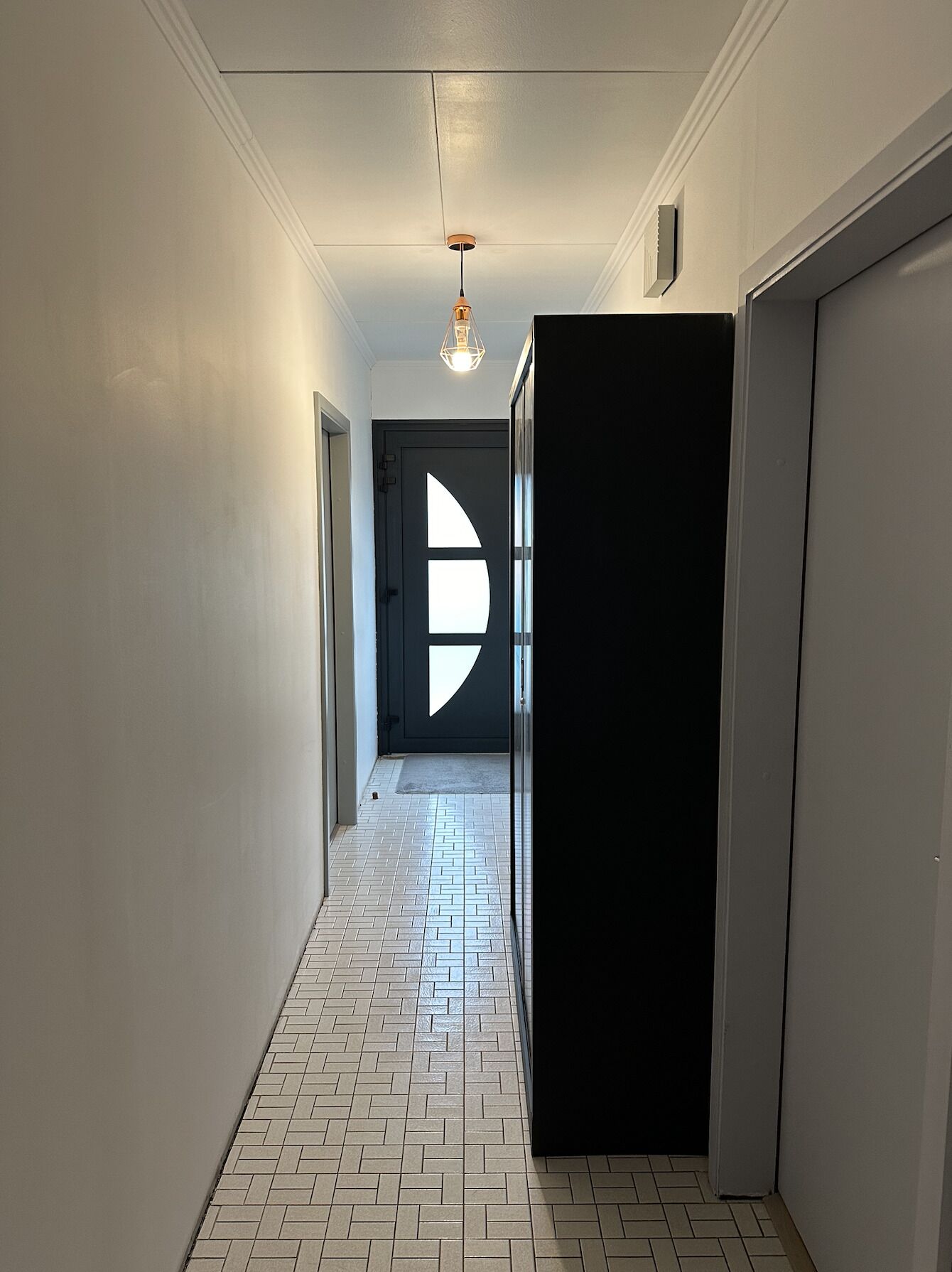 A hallway with a patterned floor, a black door with a white geometric design, and a hanging light fixture.