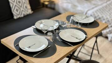 Une table à manger élégamment dressée, avec des assiettes, des couverts et des verres, placée dans une pièce moderne où l’on aperçoit un canapé et une lampe en arrière-plan.