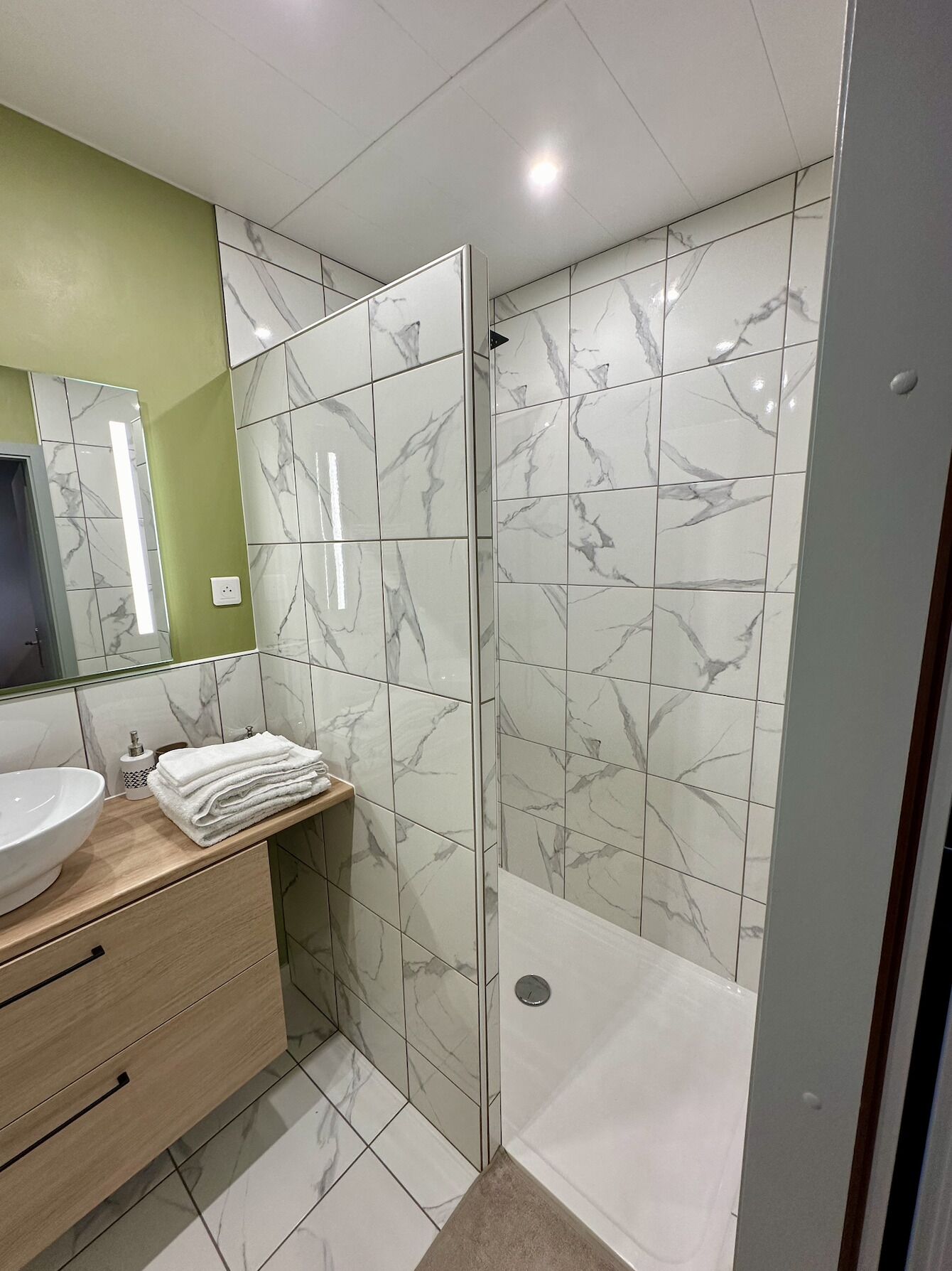 A modern bathroom with a marble-tiled shower enclosure, a wooden vanity with a sink, and a mirror.