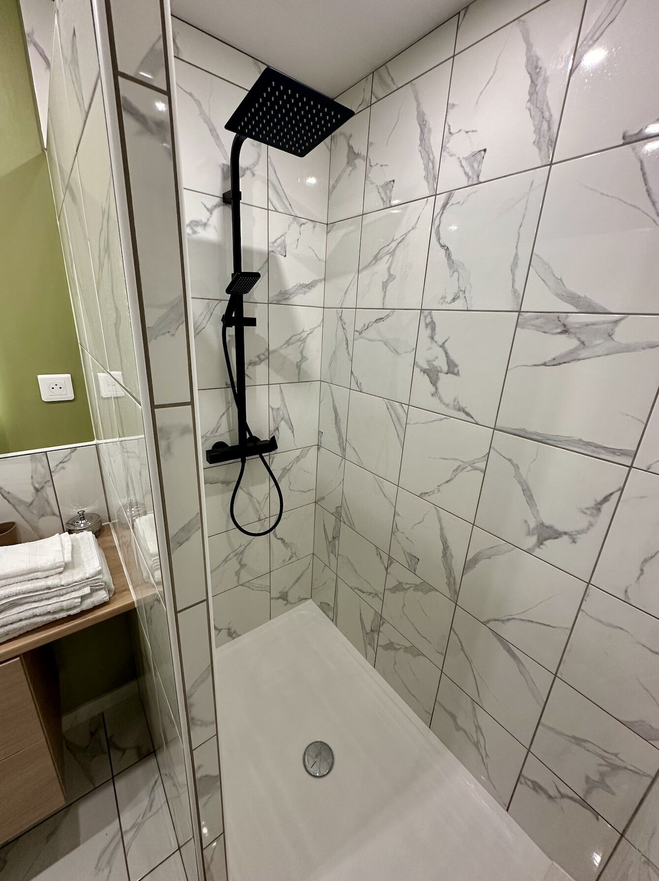 Une douche moderne dotée d’un pommeau de douche carré, d’un pommeau de douche à main et d’un panneau de commande.