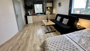 A compact living space with a kitchenette, a sofa, a dining table, and a large window providing a view of the outdoors.