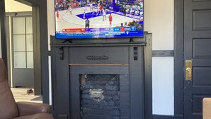 A living room with a large flat-screen TV mounted above a fireplace, a brown leather chair, and a remote control on a black ottoman. - Downtown Danville Luxury House, walk to restaurants & bars, dog friendly (Danville)