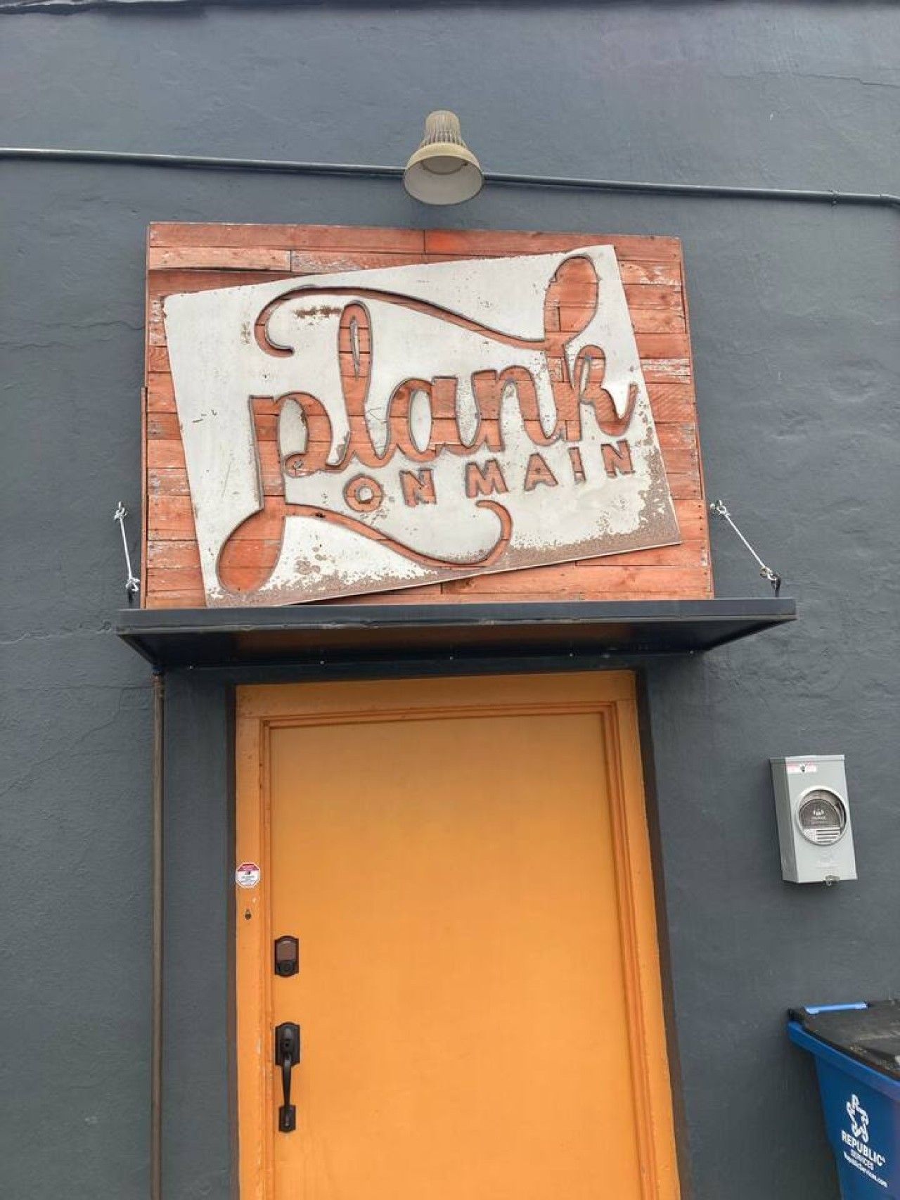 Een gebouw met een bord waarop 'Plank on Main' staat en een gele deur.