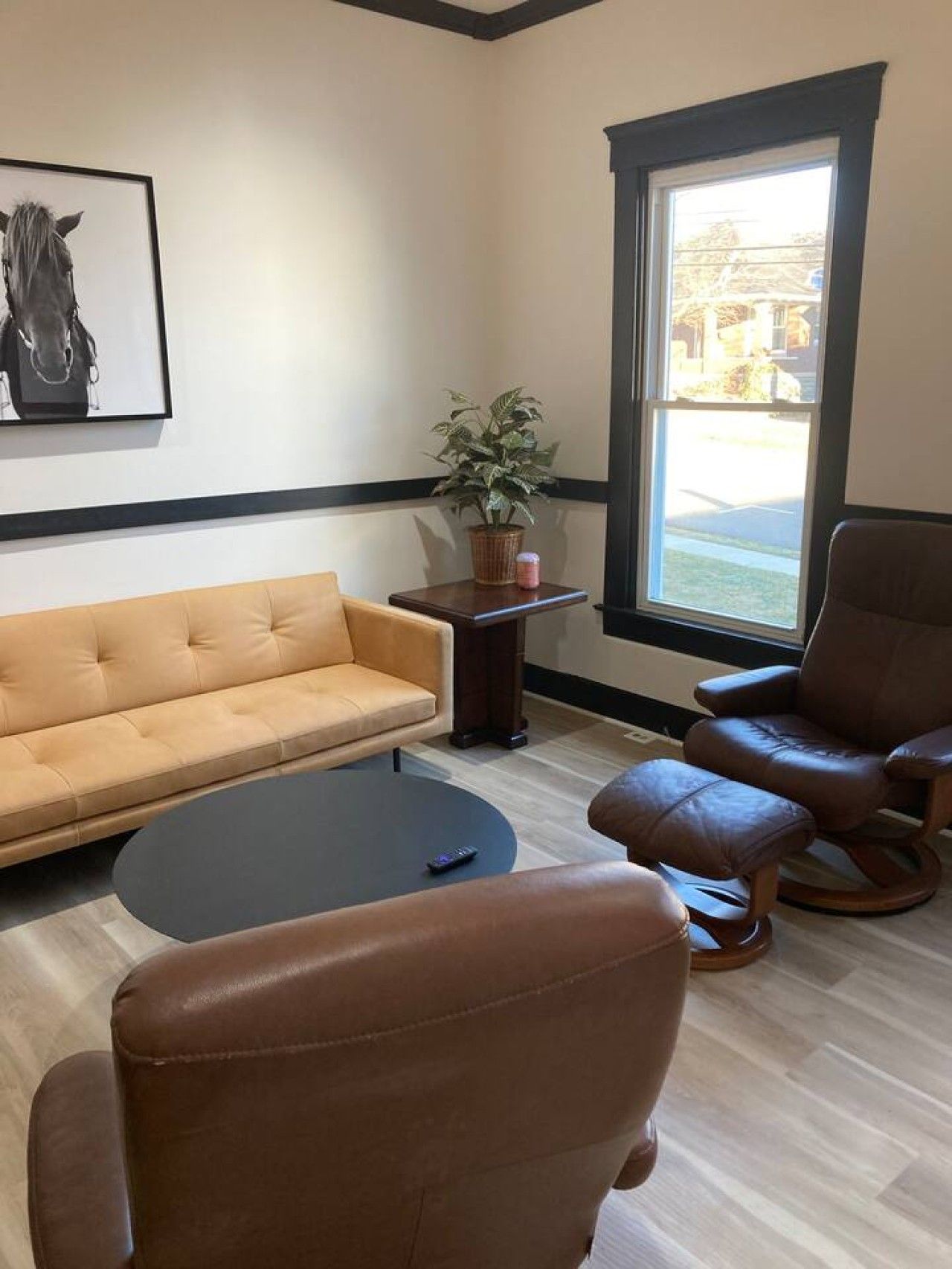 Una sala de estar con un sofá, dos sillones, una mesa de centro, una planta en maceta y una ventana con vistas.