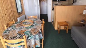 Una habitación con una mesa de comedor, sillas, una cama, un rincón de cocina y una puerta que da a otra habitación.