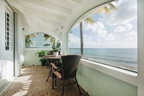 A covered outdoor area with a table and chairs, potted plants, and a view of the ocean.