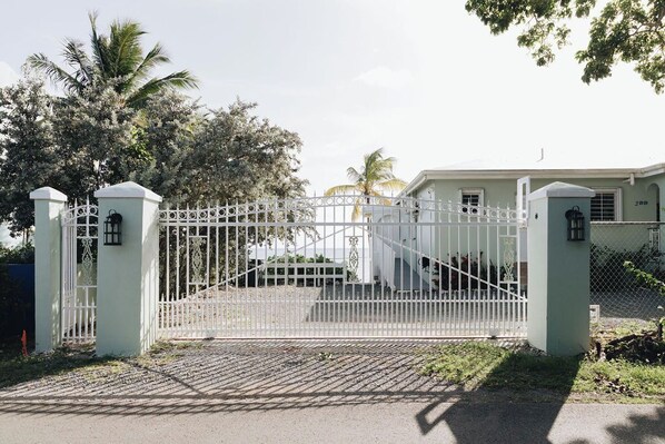 A gated entrance with a white fence, a staircase leading to a building, and palm trees in the background.