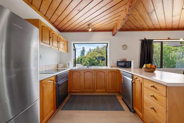 A modern kitchen with wooden cabinets, stainless steel appliances, and a view of greenery outside.