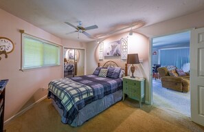 A bedroom with a bed, bedside tables, a ceiling fan, and a view into another room.