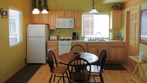 A compact kitchen with wooden cabinets, a refrigerator, a microwave, a stove, and a dining table with chairs. - Cabin on the Kenai River (Soldotna)