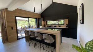 Una cocina moderna con una isla central, taburetes de bar, un salpicadero negro y una ventana con vistas a zonas verdes.