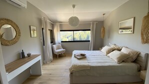 Un dormitorio con una cama grande, una mesita de noche, una silla y una ventana con vistas a árboles.