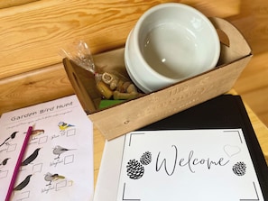 A wooden box with a white bowl, a bird-themed paper, and a welcome sign with pinecones. - Pine Lodge - UK46279 (Camerton, near Bath)