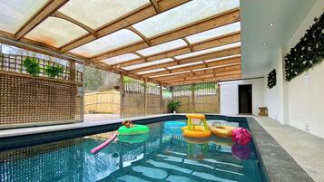 A swimming pool with a wooden ceiling and glass panels, surrounded by a wooden fence and plants.