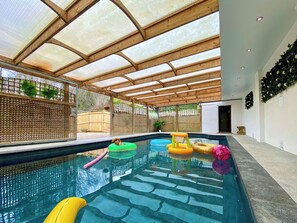 A swimming pool with a wooden ceiling and glass panels, surrounded by a wooden fence and plants. - Pine Lodge - UK46279 (Camerton, near Bath)