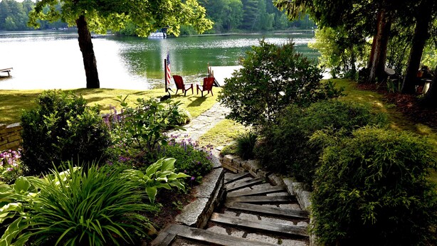 A stone staircase leading to a grassy area with red chairs and an American flag, overlooking a lake. - Waterfront house on Miner Lake- Waupaca Chain (Waupaca)