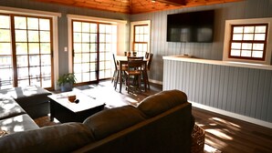 A cozy living room with a wooden ceiling, a dining area with a table and chairs, and large windows allowing natural light. - Waterfront house on Miner Lake- Waupaca Chain (Waupaca)