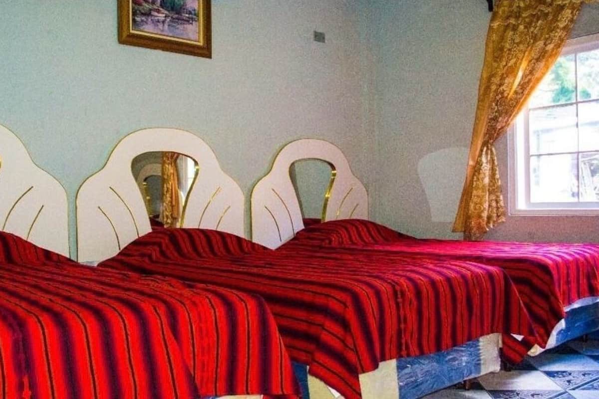 A room with two beds with white headboards and red bedding.