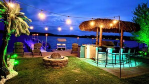 An outdoor patio area with string lights, a thatched umbrella, and a pool. - Lincoln Lake Paradise with Tiki Bar & Hot Tub (Gowen)