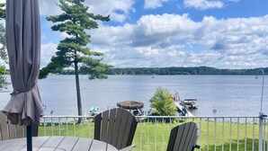 A deck with a round table and chairs, overlooking a lake with boats and a grassy area. - Lincoln Lake Paradise with Tiki Bar & Hot Tub (Gowen)
