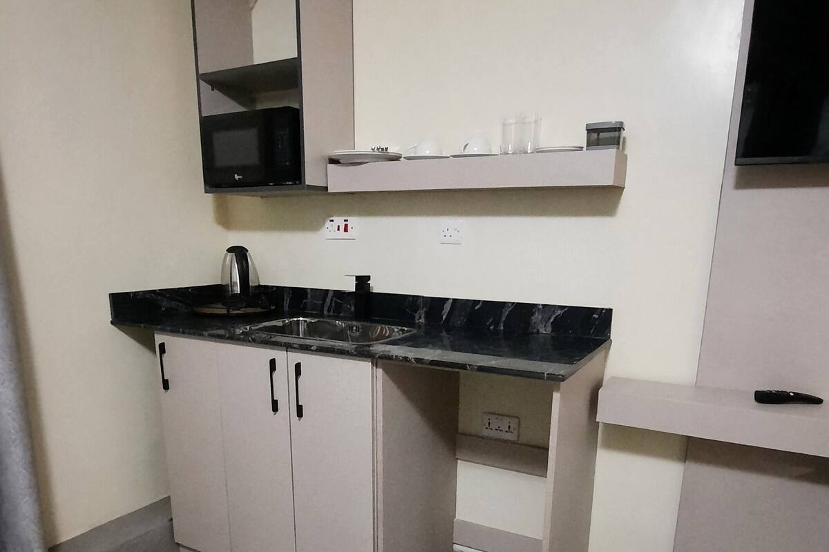 Cocina compacta con encimera negra, armarios blancos y microondas integrado.