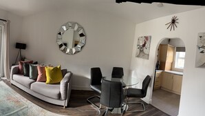 Una sala de estar moderna con un sofá, una mesa de centro de vidrio, un televisor y un comedor con sillas y una mesa.