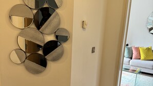 Un pasillo con un arreglo de espejos en la pared y una puerta que da a una sala de estar con un sofá y cojines.