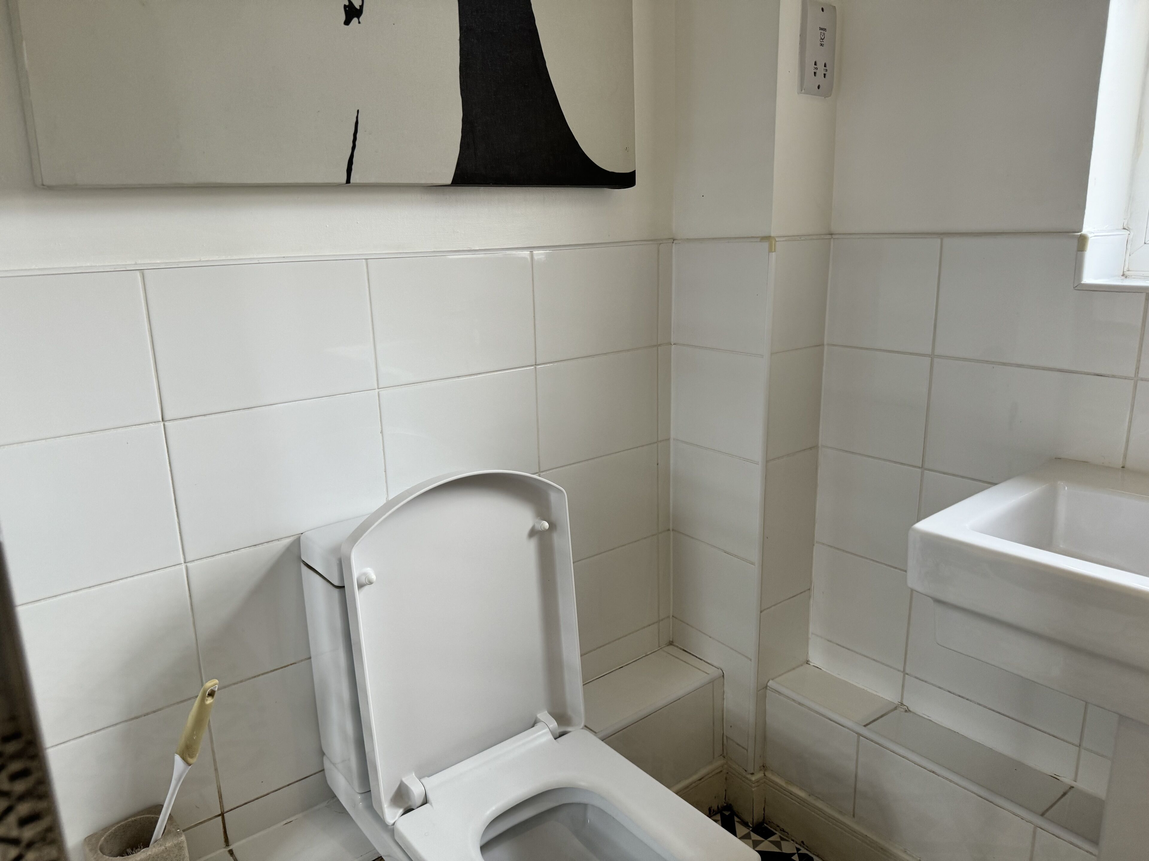 Un baño pequeño y blanco con inodoro, lavamanos y pared de azulejos.