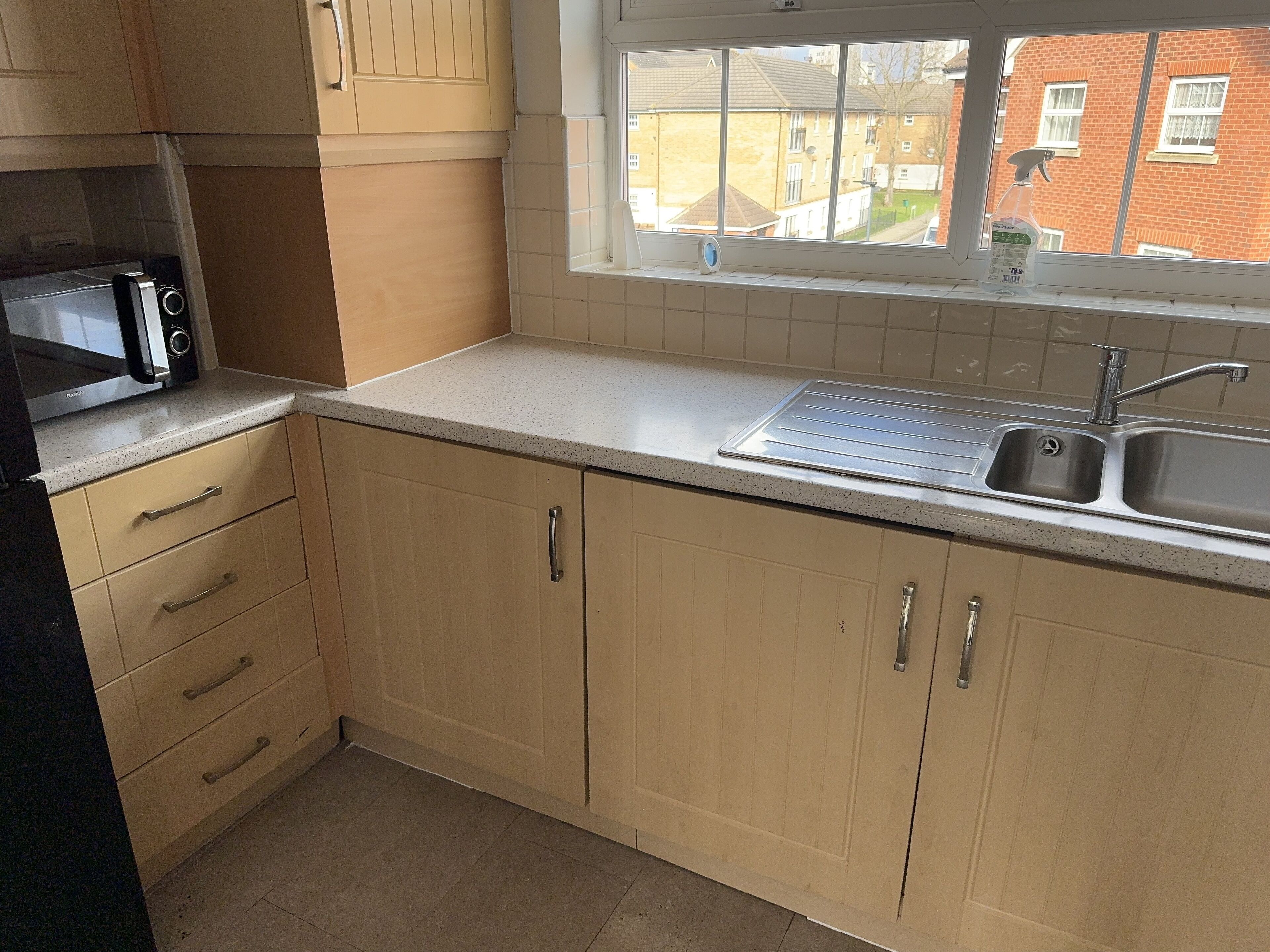 A kitchen with beige cabinets, a stainless steel sink, and a window overlooking a residential area.