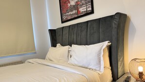 Una cama bien hecha con sábanas blancas, un cabecero oscuro y una mesita de noche con una lámpara.