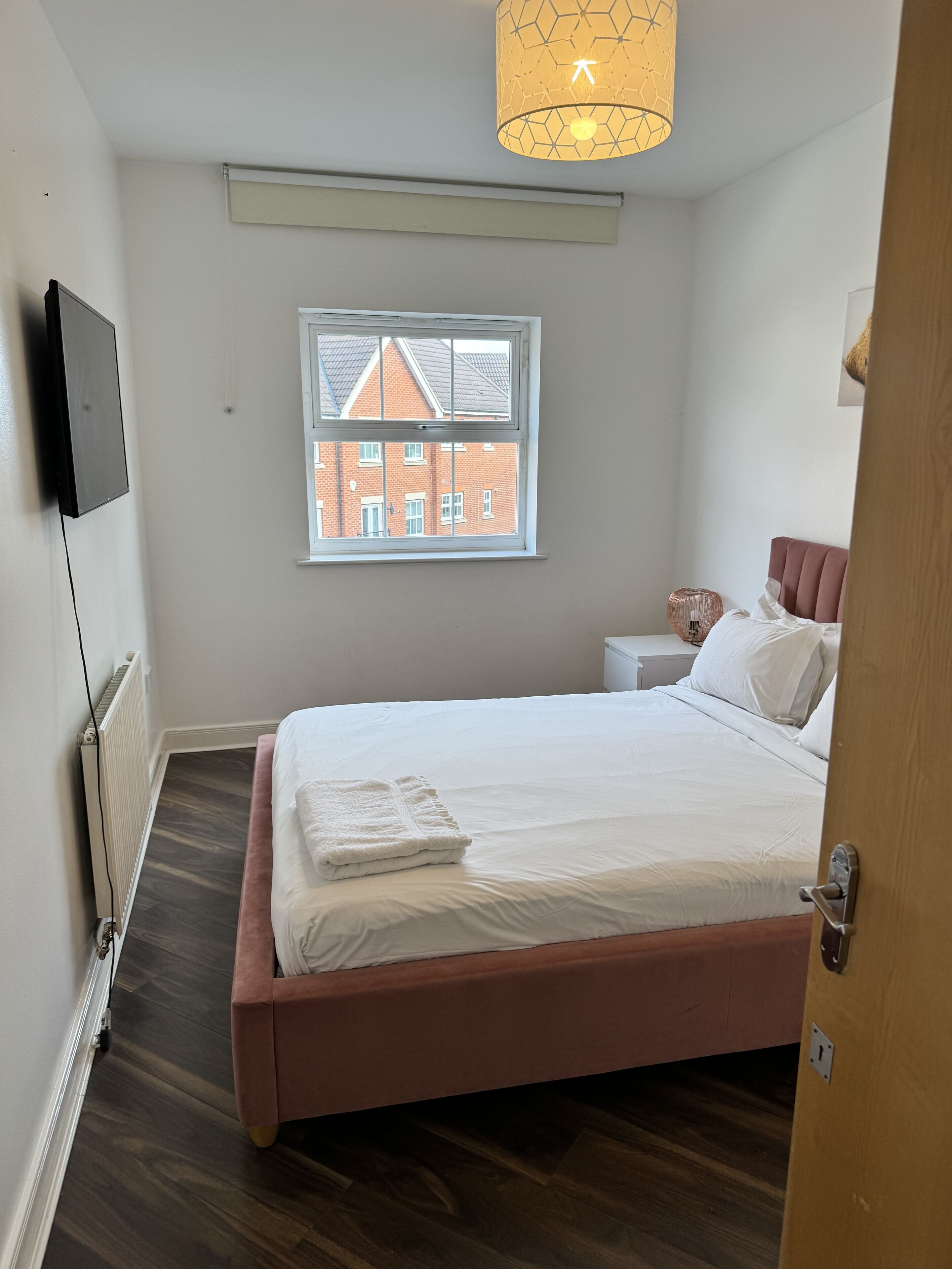 A bedroom with a bed, a window, a radiator, a TV, and a door.