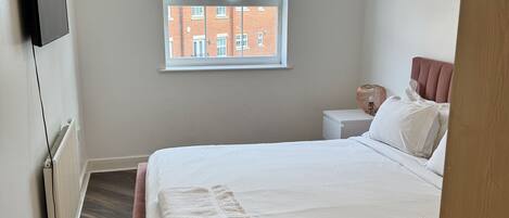 A bedroom with a bed, a window, a radiator, a TV, and a door.