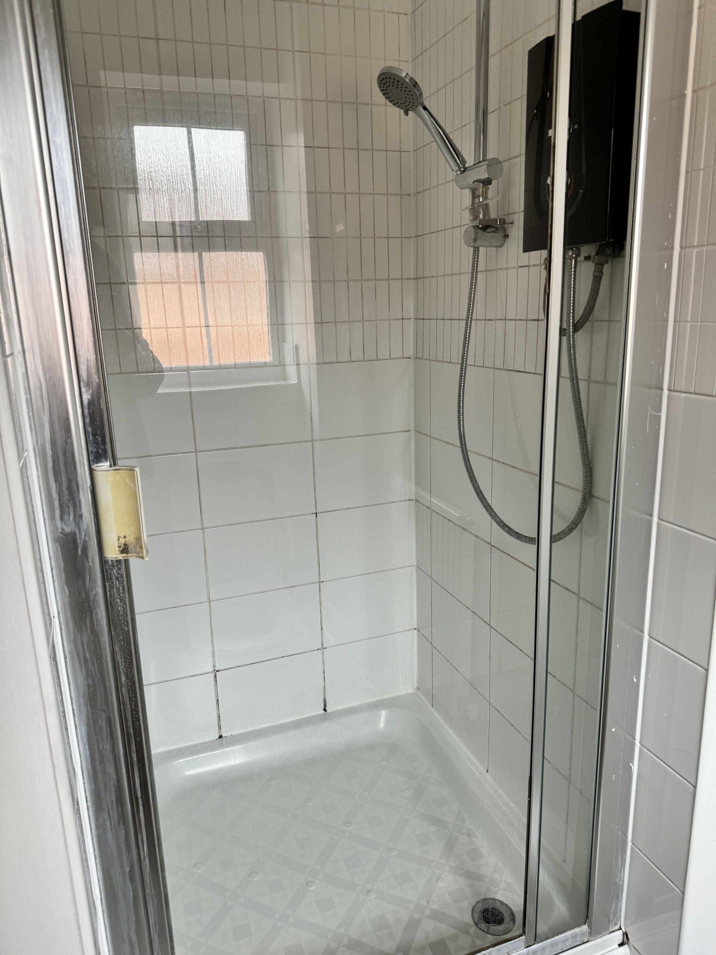 A glass-enclosed shower with white tiles, a handheld showerhead, and a handheld shower attachment.