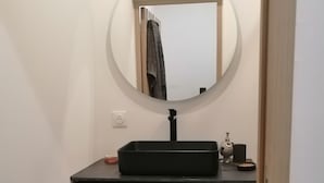 Uma casa de banho com uma toucador de madeira, um espelho redondo e uma pia preta.